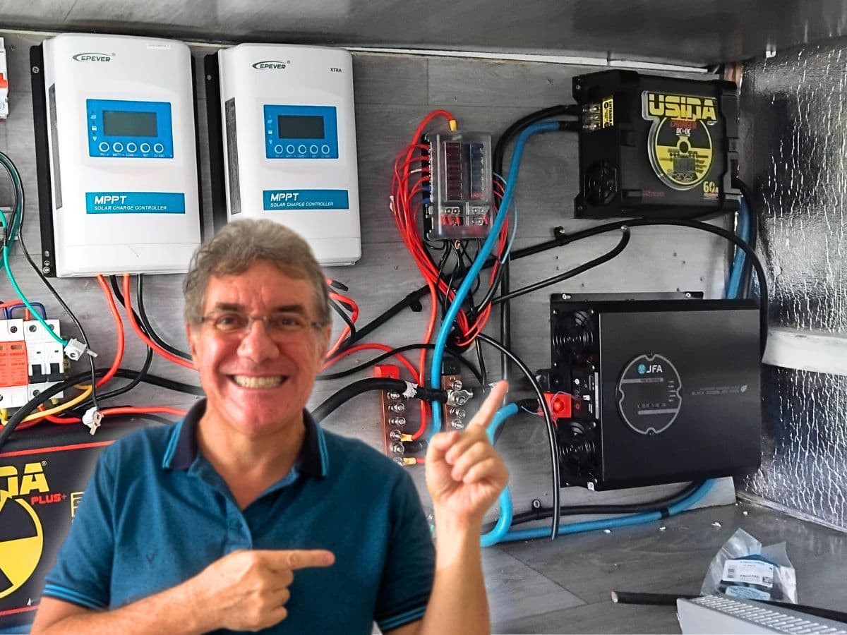 Hitner apontando para o inversor JFA Black instalado no painel elétrico do motorhome, ao lado dos controladores MPPT e do carregador DC-DC